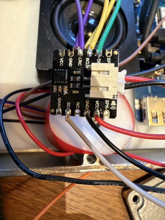 Close-up of the small black amplifier board with purple, yellow and green signal wires and red and black power wires soldered on