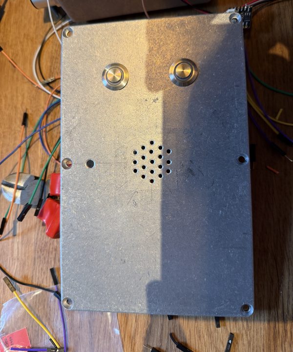 The aluminium lid with two stainless push buttons fitted and a drilled hexagonal speaker grille
